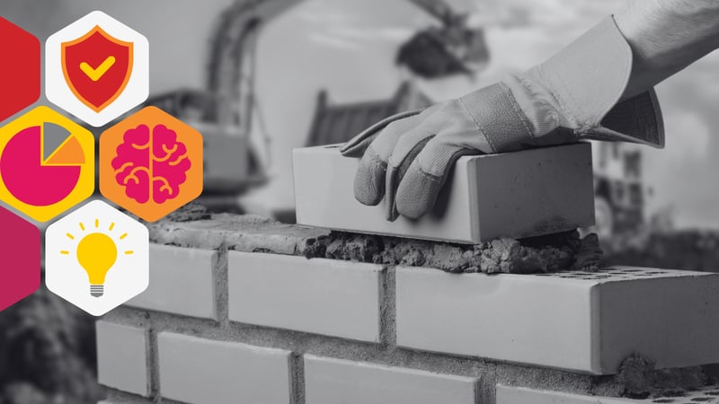 a gloved hand lays bricks in the foreground, in the background is a construction site