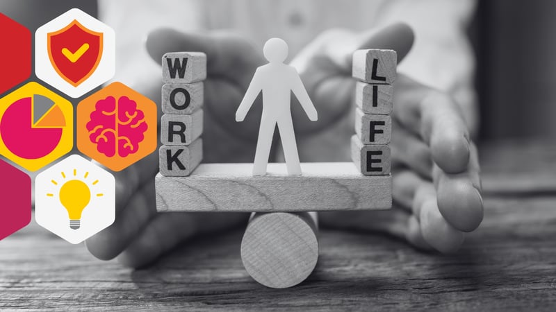 a pair of hands steadies a wooden block which balances on a wooden cylinder. On top of the wooden block is a series of alphabet blocks which spell 'work' and 'life' in between the stacks of blocks, a stick figure toy stands.