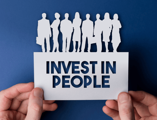 a pair of hands holds a paper cutout that says Invest in People