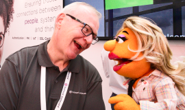 Photograph of a female puppet smiling with a human male during an interview
